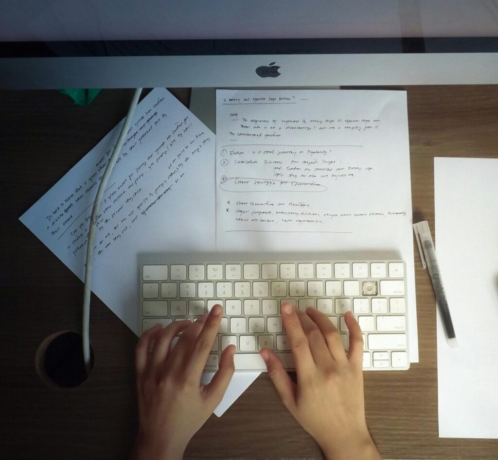 Hands typing on a keyboard at a wooden desk with papers and computer mouse visible.